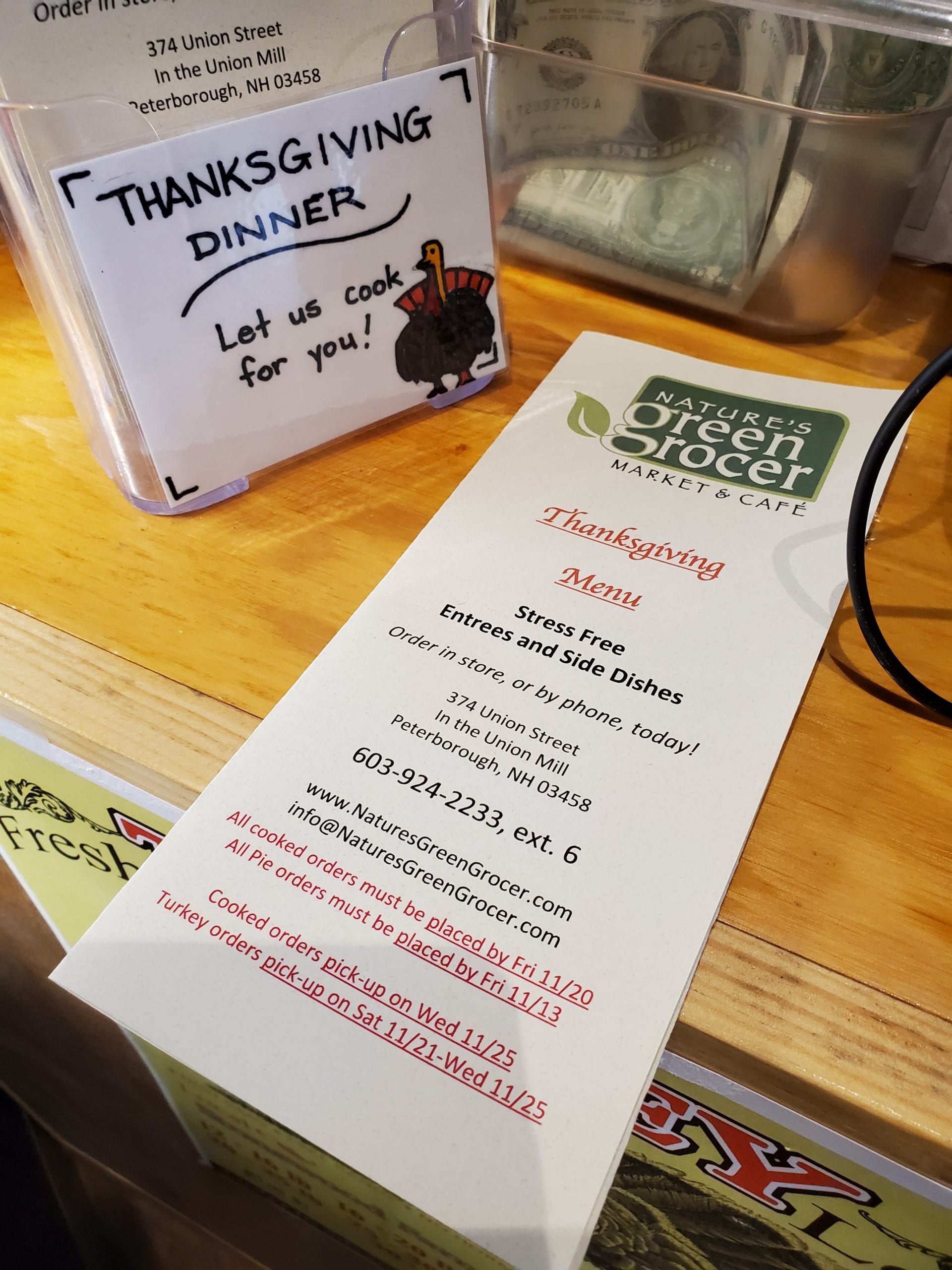 A folded menu of Thanksgiving dinner options at Green Grocer on a counter with a sign that reads 'let us cook for you!'