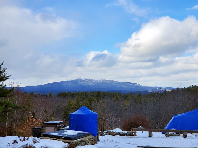 Mount Monadnock against a semi cloudy sky in the background while blue tents and stone benches are in the foreground