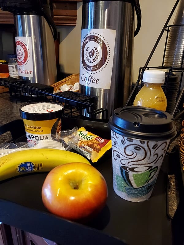 A tray with fruit, juice, coffee and oatmeal sits in front of a coffee carafe