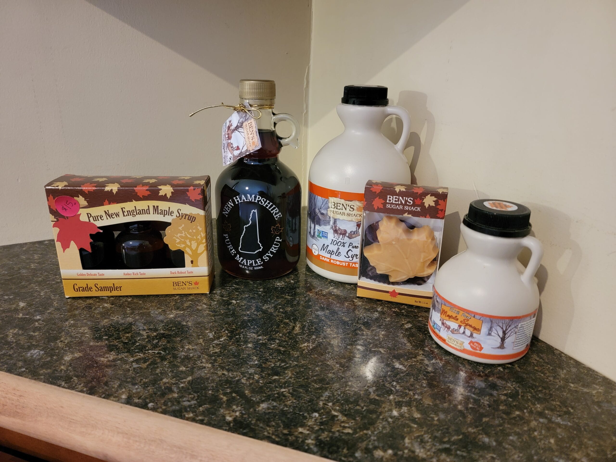 Various types of maple products are displayed on a marble countertop, including syrup, samplers, and maple candy.