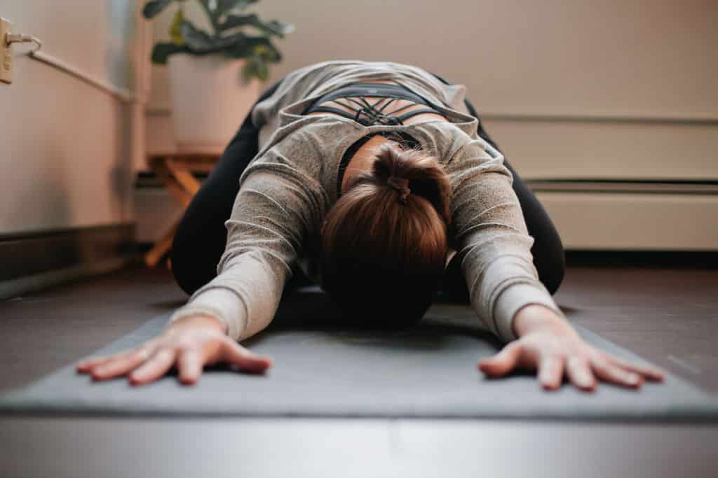 woman bows head in yoga pose on a mat, hands stretched forward