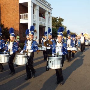 Drummers and other band members in blue and white uniforms march in formation