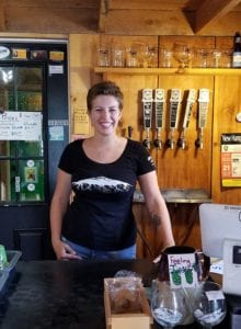 Young woman standing behind counter with beer taps behind