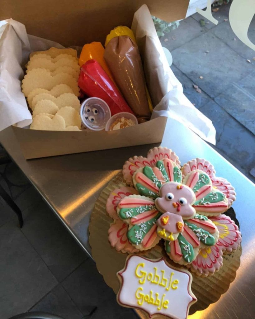 A box with sugar cookies and decorating supplies sits off to the side while a fully constructed cookie turkey is in front of it.