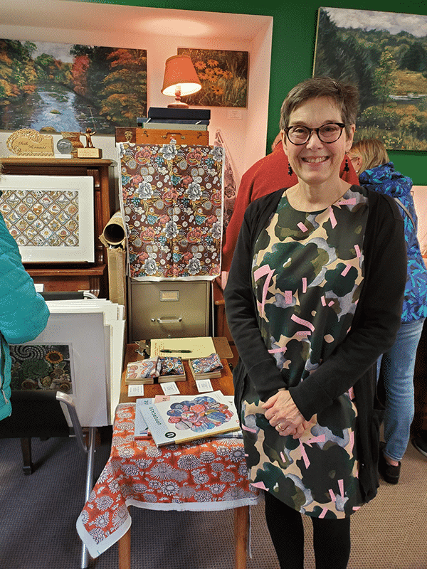 Artist Beth Krommes stands in front of a table draped with her textile work.