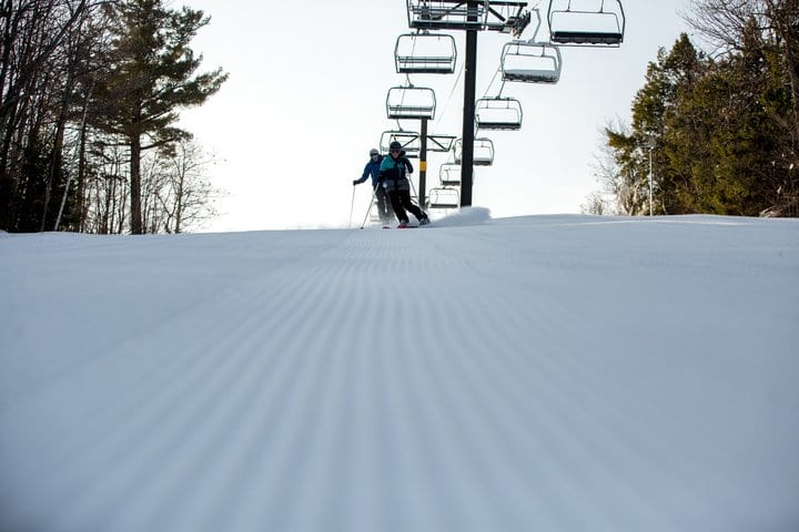 skiers coming down a freshly groomed slope with the ski lift behind them.