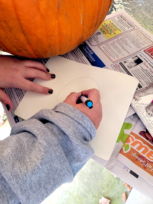 Someone begins to sketch out a design for their pumpkin on a piece of paper