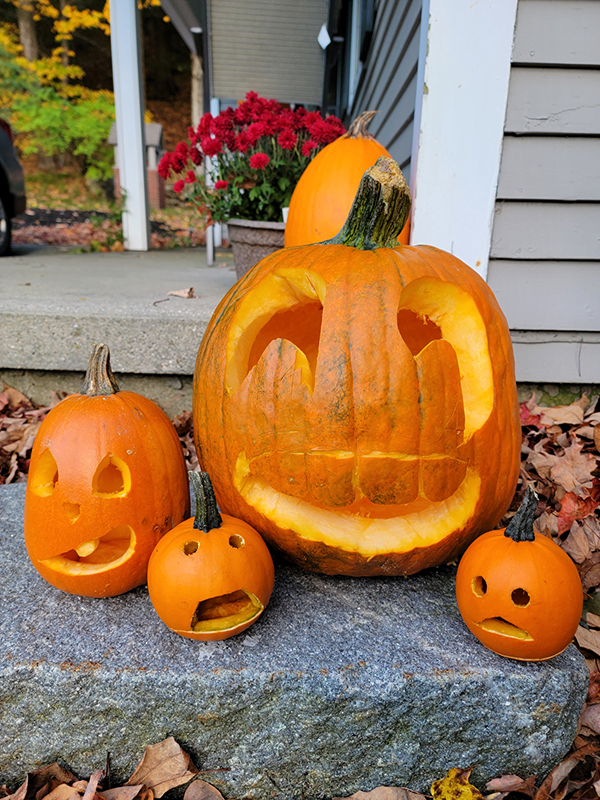 four pumpkins of varying size sit on a step with faces carved into them