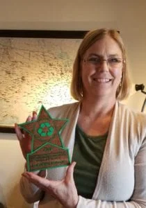 Woman holding up a wood star colored green with recycling symbol