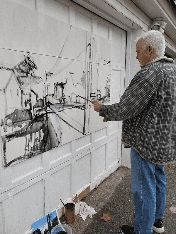 Artist Kris Calnan focuses on the canvas hung on the garage door, painting with black paint.
