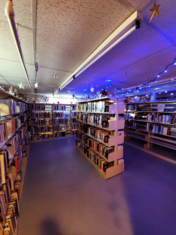 A dim room of library bookshelves with blue christmas lights on the ceiling