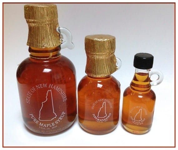 three different sized glass bottles of maple syrup are arranged on a white background with the state of New Hampshire printed on the front of each
