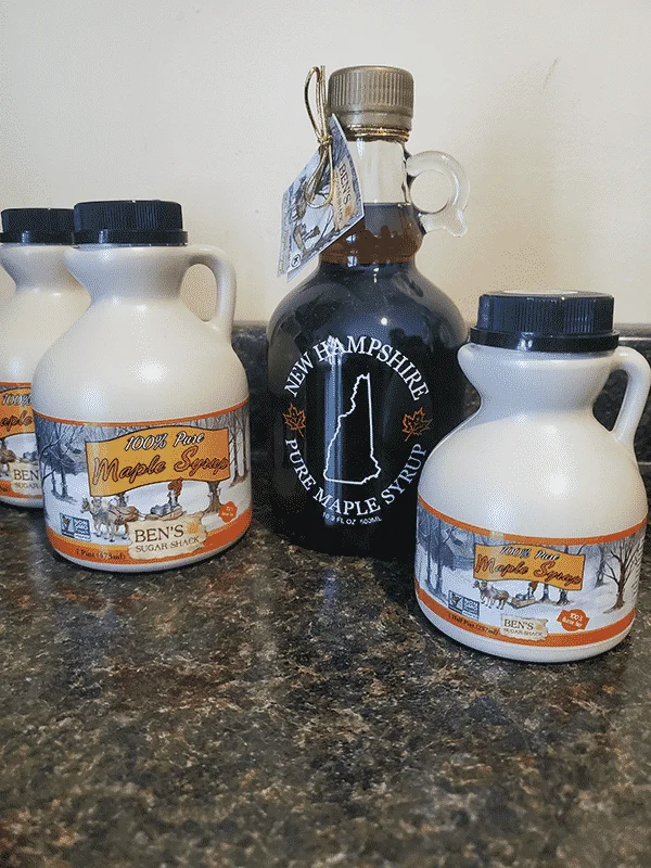 Various sizes of maple syrup jugs sit on a table, three of plastic and one of glass