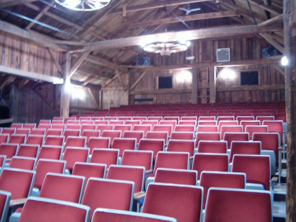 Rows of theater seats in a well lit barn playhouse.