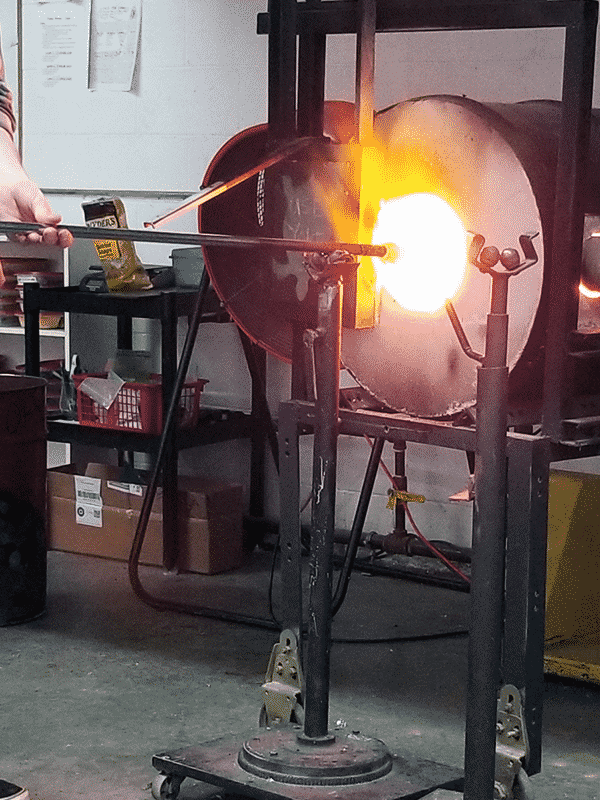 a large furnace for glassblowing heats up molten glass on the end of a metal pipe.