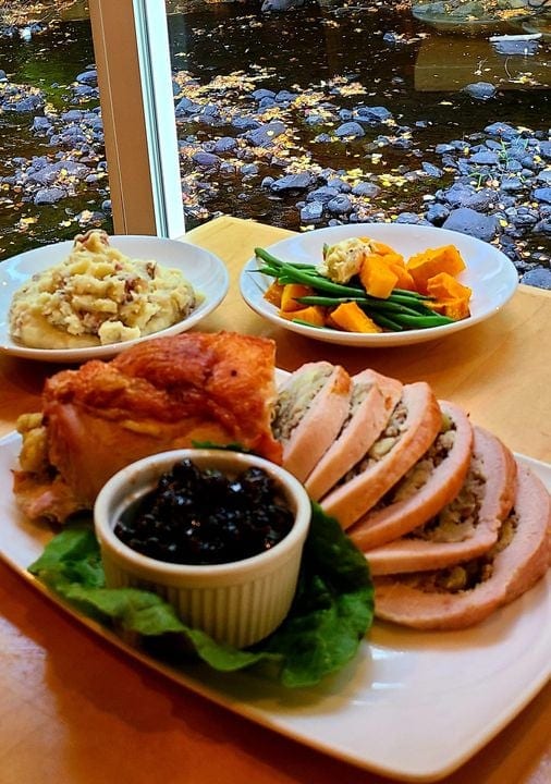 Spread of stuffed turkey breast, cranberry sauce, sauteed veggies and mashed potatoes on a table overlooking the river at Waterhouse Restaurant